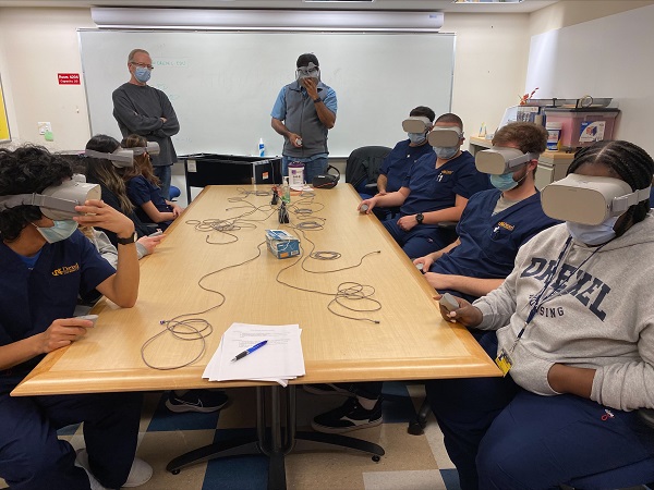 Drexel undergraduate nursing students sitting around a table wearing virtual reality goggles for a simulation in their Health Assessment course.